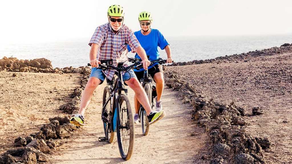 Older couple outside riding electric bikes on a dirt trail.