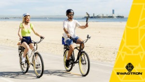 Happy couple wearing helmets, riding their electric bikes along the beachside boardwalk.