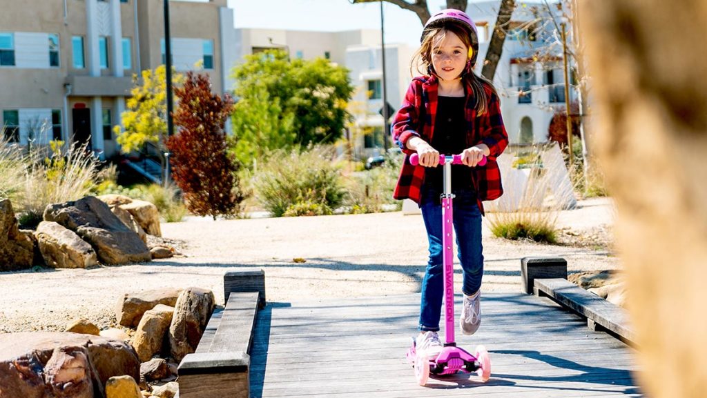 Girl wearing helmet riding a K5 3-wheeled light-up kick scooter.