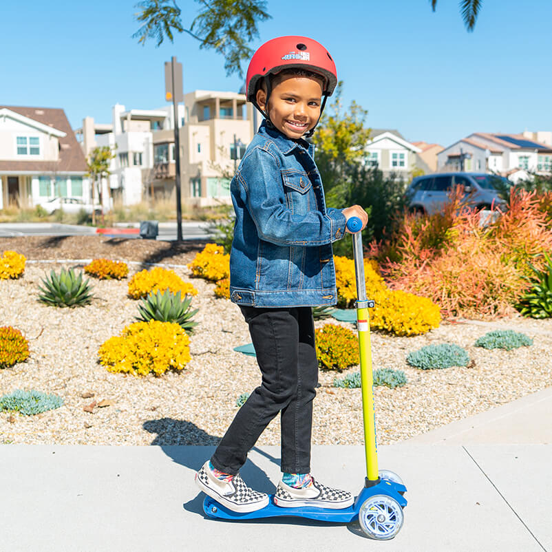 Kid in the park riding his blue three-wheel kick scooter