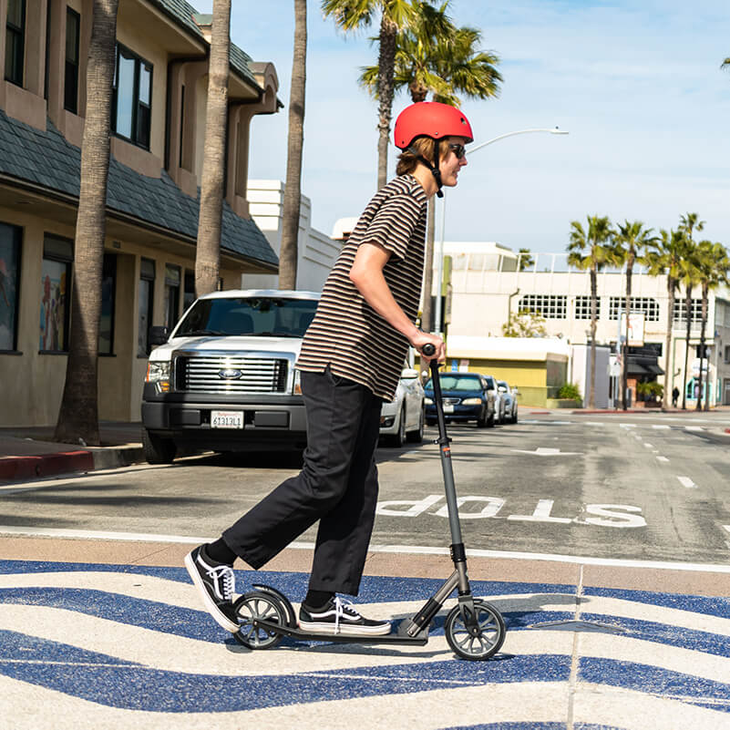 Boy crosses the street while riding on his kick scooter