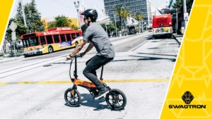 Young man wearing a helmet, riding an EB7 Pro Electric Bike across the street.