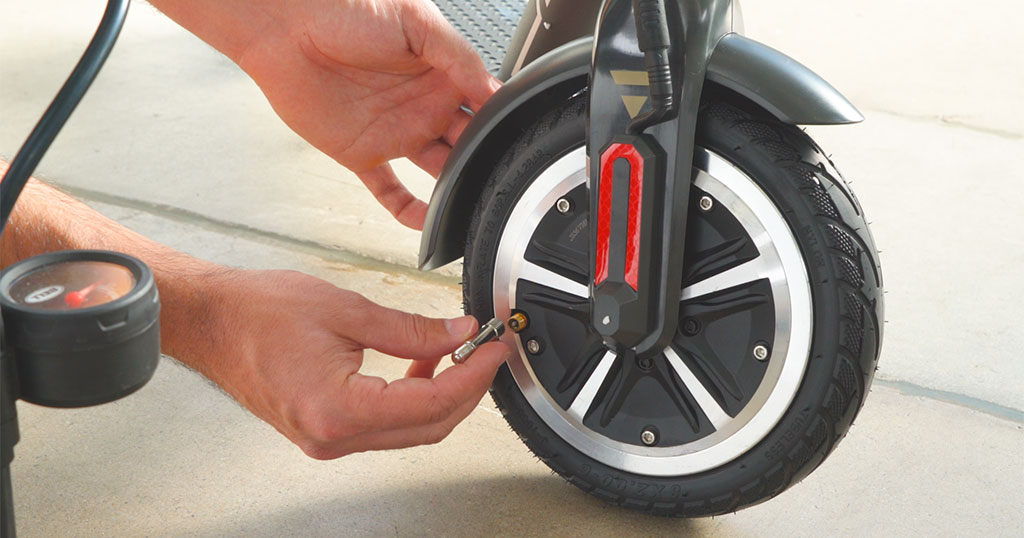 Close-up of guy using a valve extender on the front tire of a Swagger 5 Elite electric scooter.