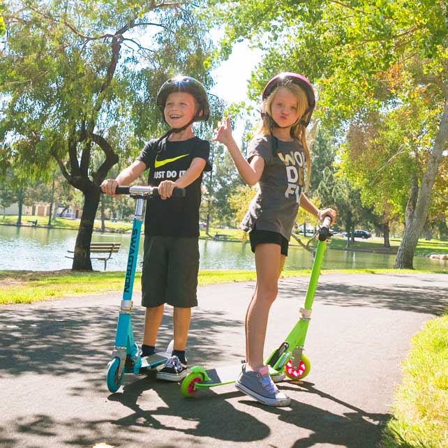 two kids play on green and blue stunt scooters