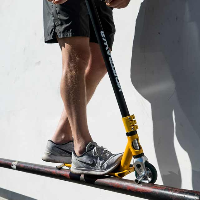 man in athletic shoes rides stunt scooter on rail