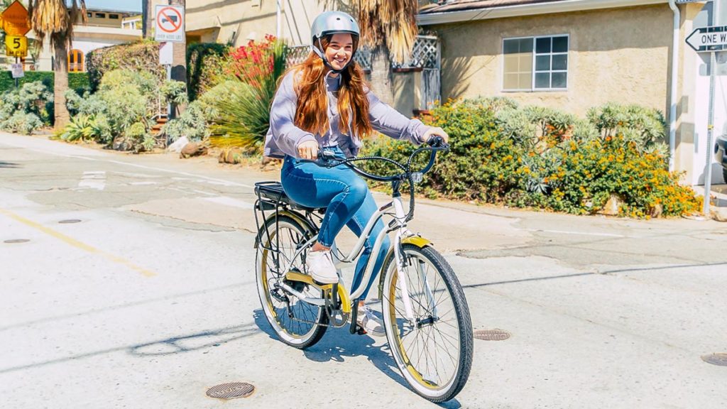 Young woman wearing a helmet riding a white EB9 Step-Through Electric City Bike.