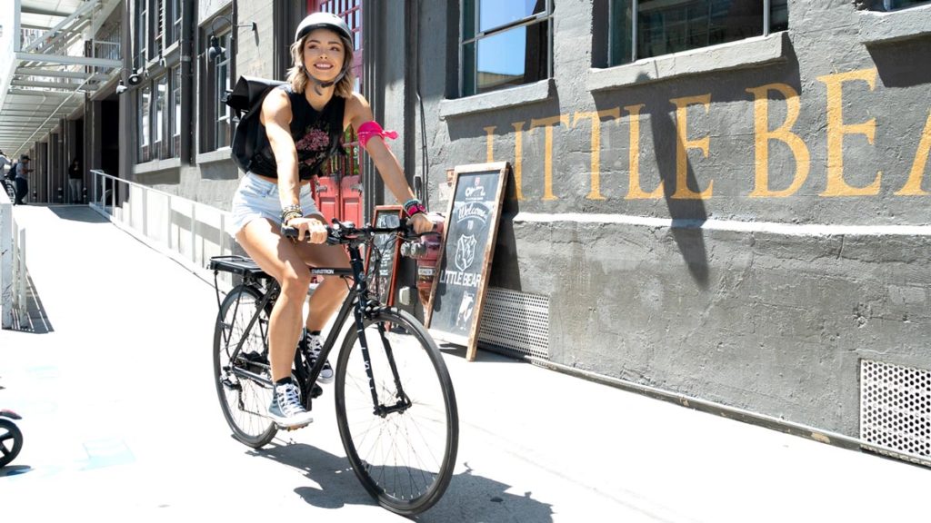 Woman wearing a helmet riding an EB12 electric bike on the sidewalk.