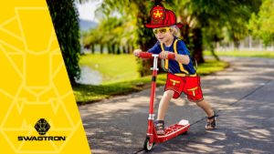 Young kid riding an SK1 Discovery kick-start scooter on the sidewalk.