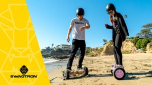 Guy and girl on the beach wearing helmets and riding the swagBOARD T6 hoverboard.