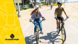 Couple wearing helmets riding their EB11 and EB10 eBikes on the boardwalk next to the beach.