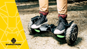 Closeup of someone standing on a black T8 hoverboard on a dirt trail.